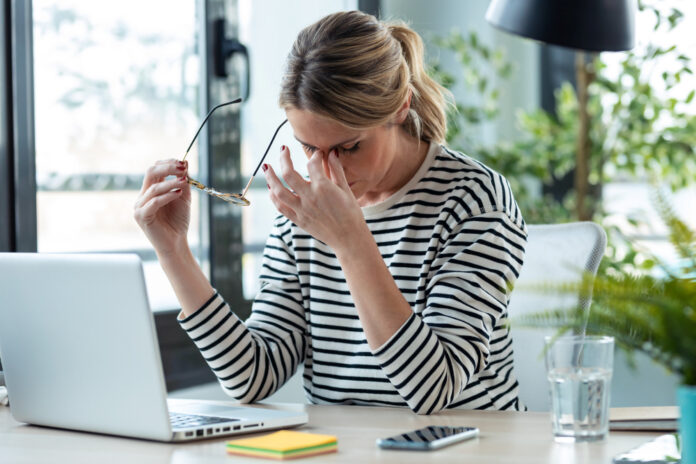 Stressed mature business woman looking worried, tired and overwhelmed while working with laptop on a desk in the office at home.
